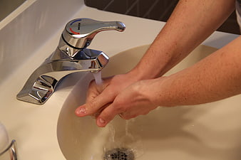 Person washing hands under running water from a chrome bathroom faucet