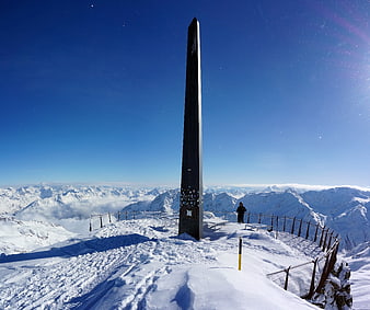Snowy mountain peak with obelisk monument and skier
