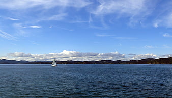 Lone Sailboat on Calm Blue Sea with Distant Hills