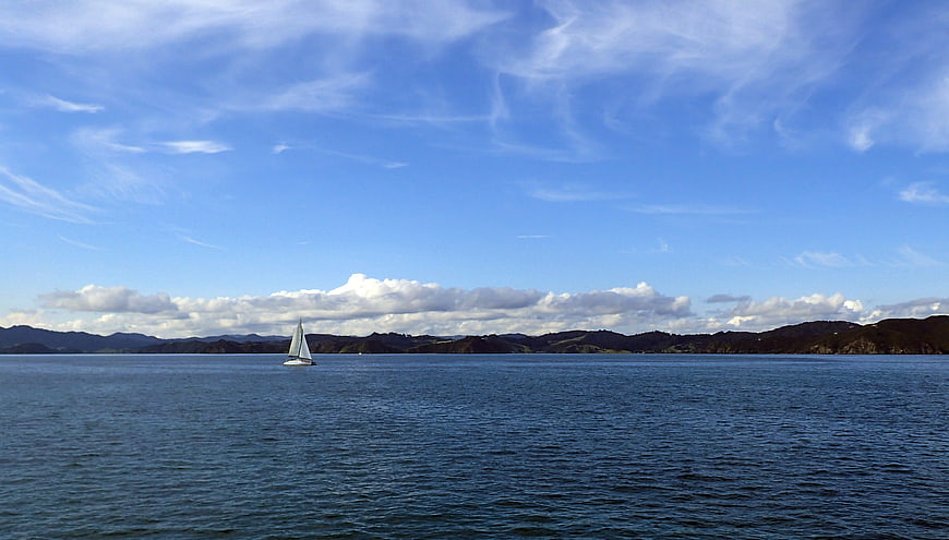 Lone Sailboat on Calm Blue Sea with Distant Hills