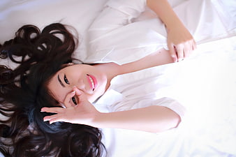 Happy Woman Lying on White Bed Making OK Sign