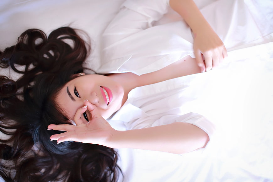 Happy Woman Lying on White Bed Making OK Sign
