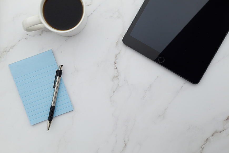 Minimalist workspace with coffee, tablet, and notepad on marble