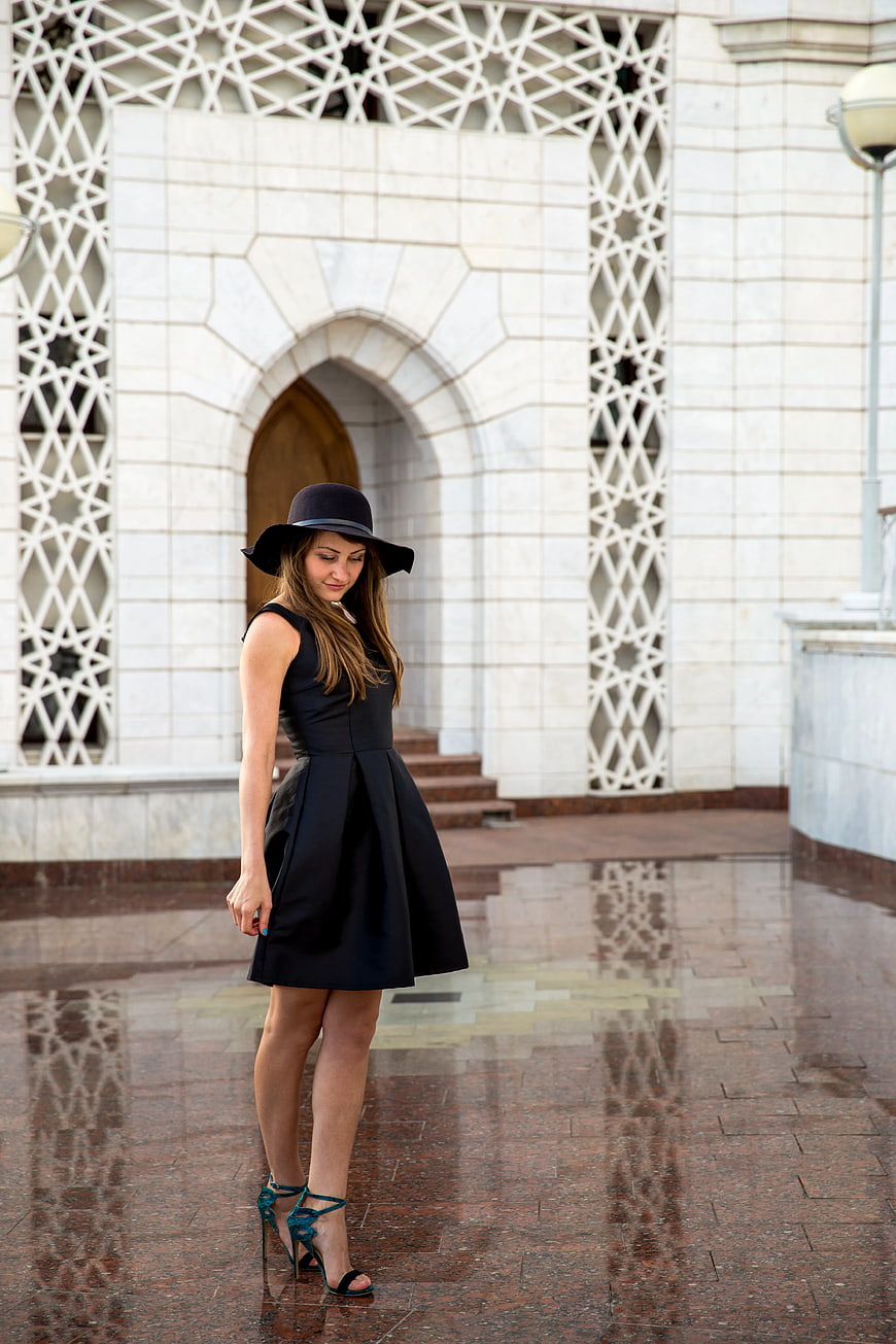Woman in Black Dress and Hat on Wet Pavement