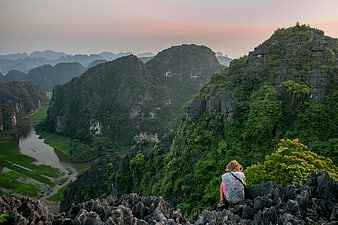 Woman sitting on rocky mountain peak overlooking river valley