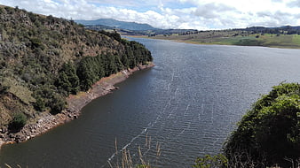 Wide view of Sisga dam reservoir with green hills and cloudy sky