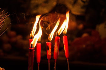 Lit red candles with tall flames and smoke in a dark temple setting