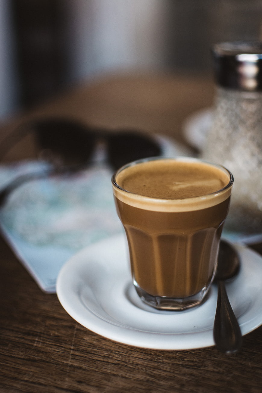Cortado coffee on wooden table with map and sunglasses