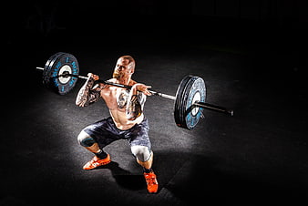Tattooed Man Performing Barbell Squat in Dark Gym