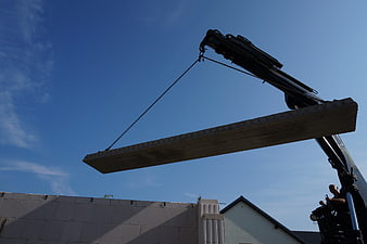 Crane lifting concrete slab against blue sky