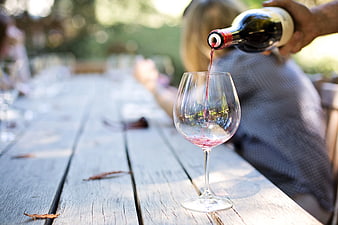 Red wine pouring into glass on rustic wooden table outdoors