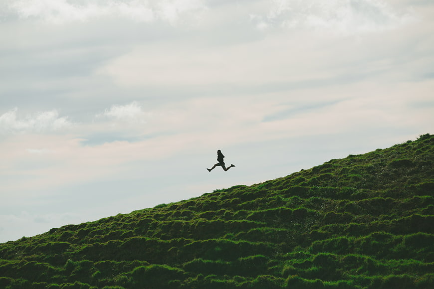 Silhouette of woman jumping on green grassy hill