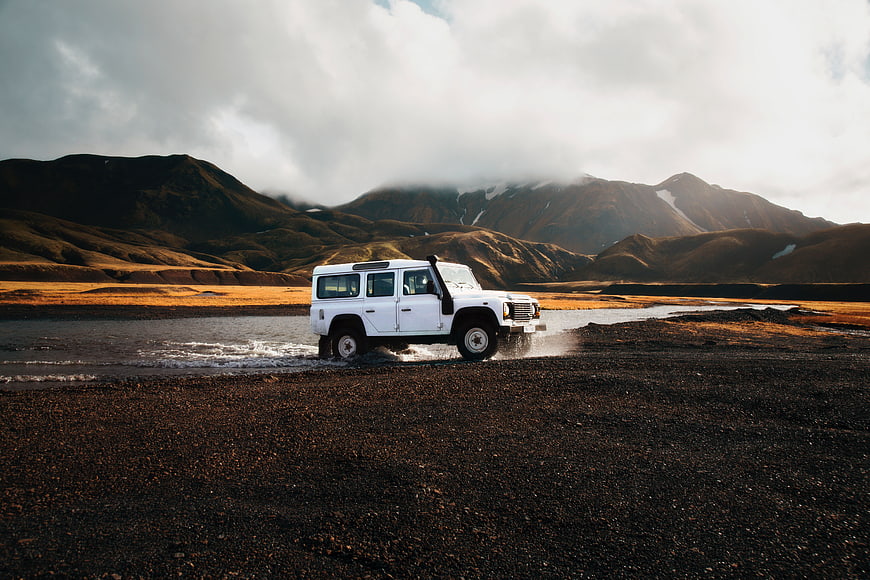 White SUV Crossing River in Mountainous Landscape