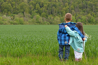 Two children standing in a green meadow with a forest background
