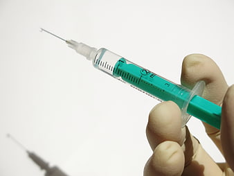 Close-up of hand holding medical syringe with green liquid