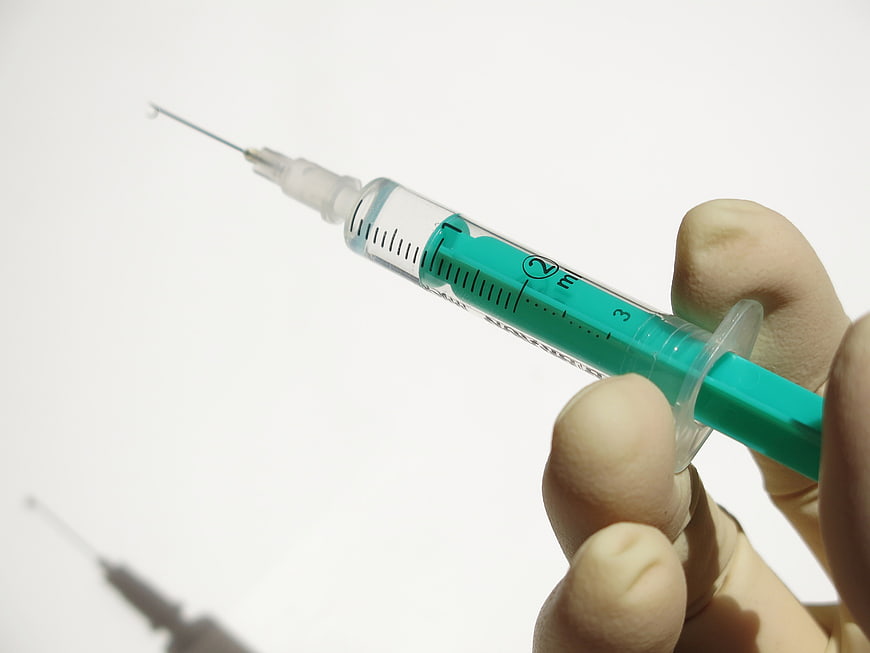 Close-up of hand holding medical syringe with green liquid