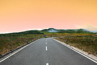 Empty asphalt road leading to misty mountains at sunset