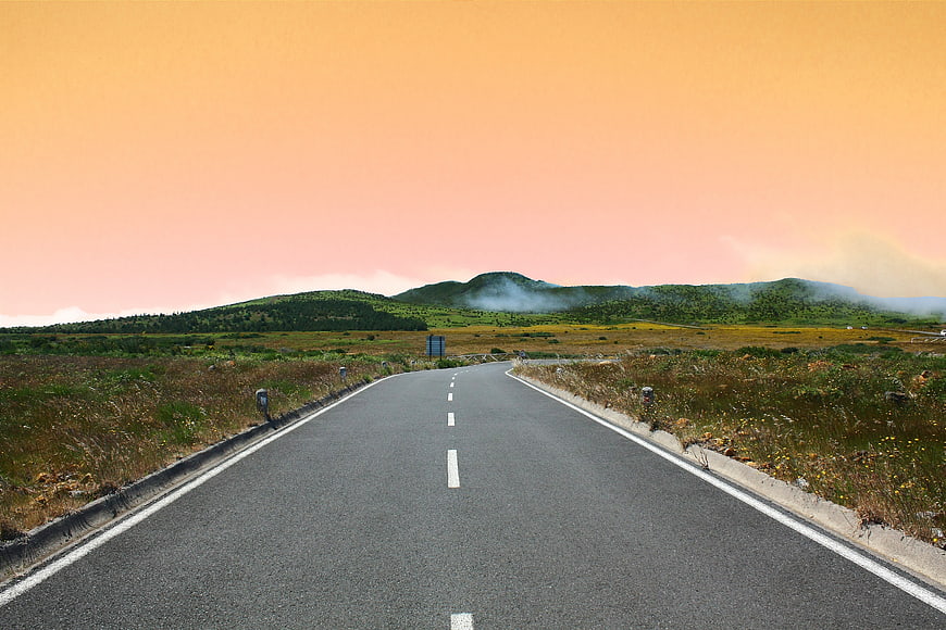 Empty asphalt road leading to misty mountains at sunset
