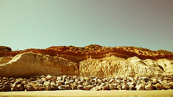 Sandy Beach with Large Rocks and Cliffs Under Blue Sky