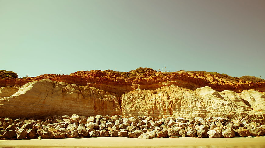 Sandy Beach with Large Rocks and Cliffs Under Blue Sky