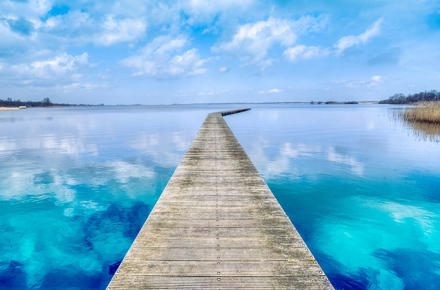 Wooden pier extending into turquoise lake with blue sky
