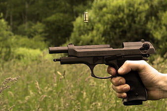 Hand holding black pistol with ejected casing in outdoor setting