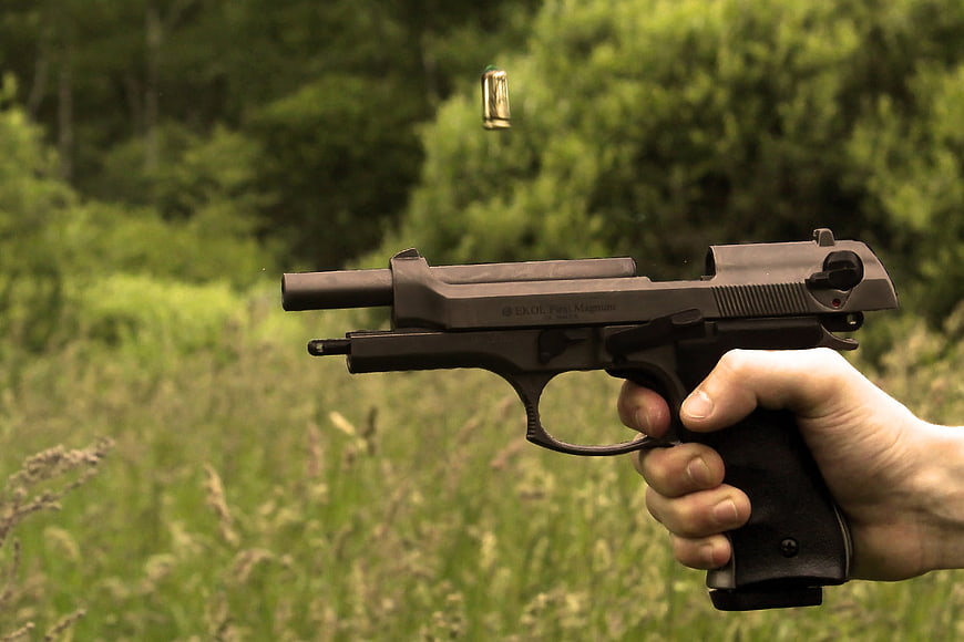 Hand holding black pistol with ejected casing in outdoor setting