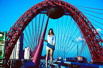 Woman standing on red bridge structure against blue sky