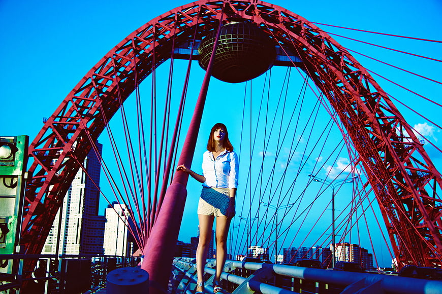 Woman standing on red bridge structure against blue sky