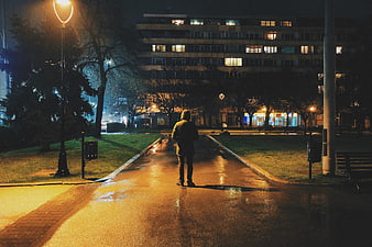 Lone Figure Walking on Wet Path at Night in Urban Park