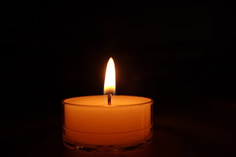 Lit tea light candle glowing warmly against a dark background