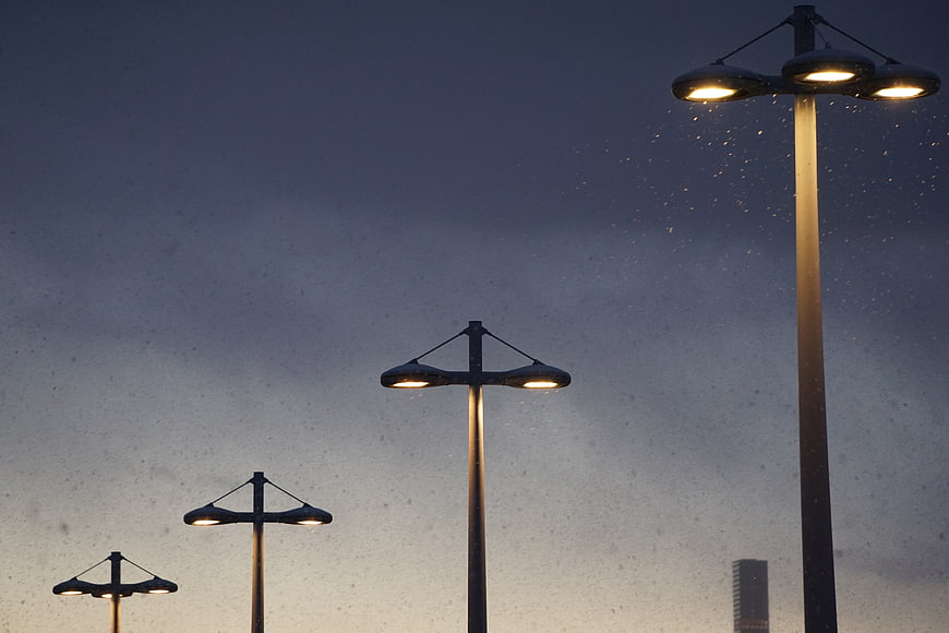 Street lamps illuminating rain against a twilight sky