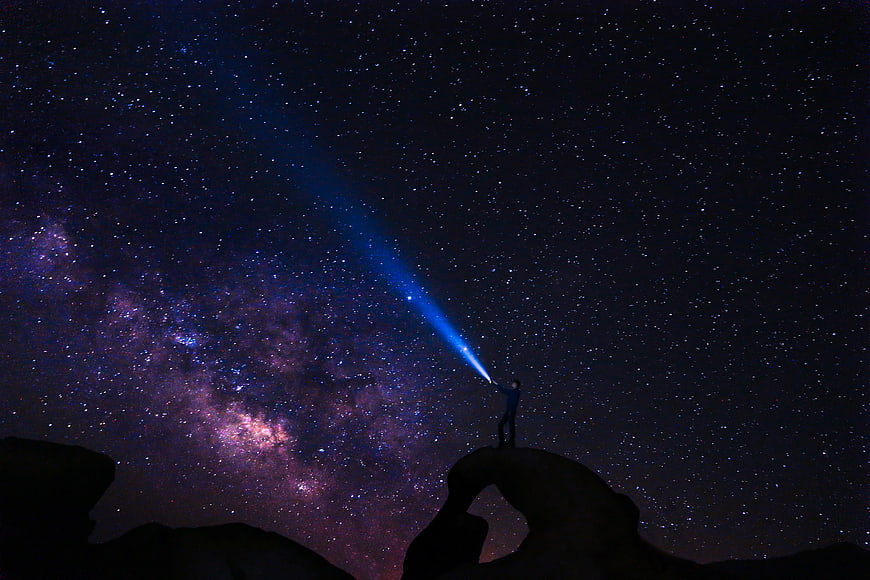 Silhouette of Man Shining Flashlight into Milky Way Galaxy