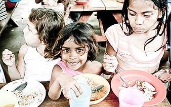 Three young children eating a meal at a wooden table