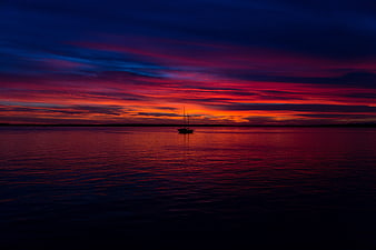 Silhouette of sailboat on calm water during vibrant sunset