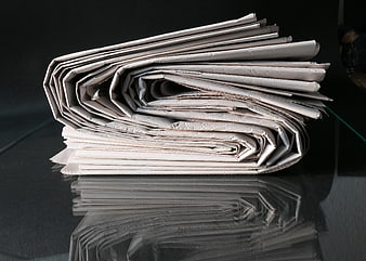Stack of folded newspapers on a reflective black surface