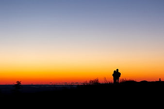 Silhouette of couple watching sunset on mountain ridge
