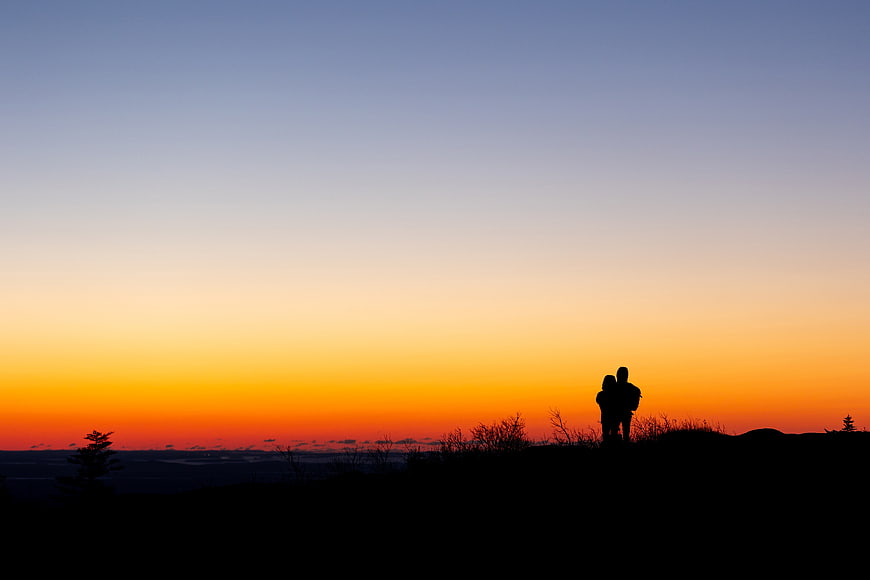 Silhouette of couple watching sunset on mountain ridge