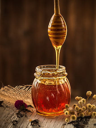Golden Honey Dripping from Wooden Dipper into Glass Jar