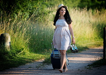 Woman walking barefoot with suitcase on country path
