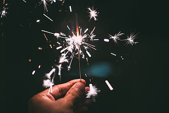 Hand holding a lit sparkler with bright sparks against a dark background