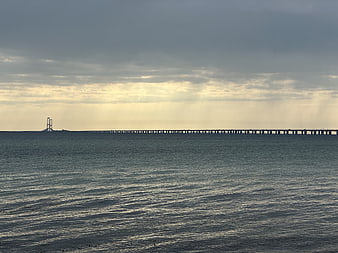 Long bridge over ocean with dramatic cloudy sky and sun rays