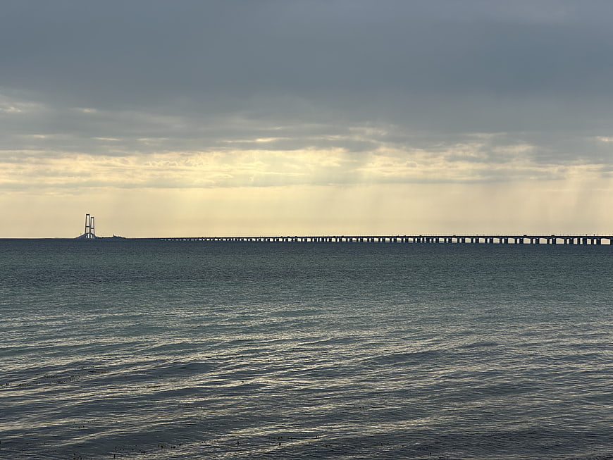 Long bridge over ocean with dramatic cloudy sky and sun rays