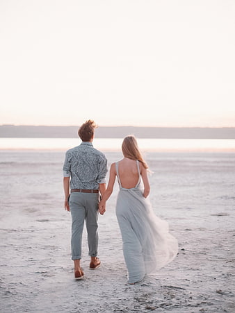 Couple Walking Hand in Hand on Sandy Beach at Sunset