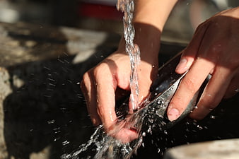 Close-up of hands washing a metal bowl with running water