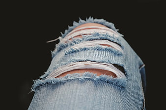 Close-up of ripped blue denim jeans on dark background