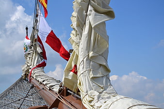 Sails and Flags on a Tall Ship Mast Against Blue Sky