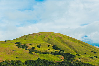 Lush green rolling hills under a cloudy blue sky