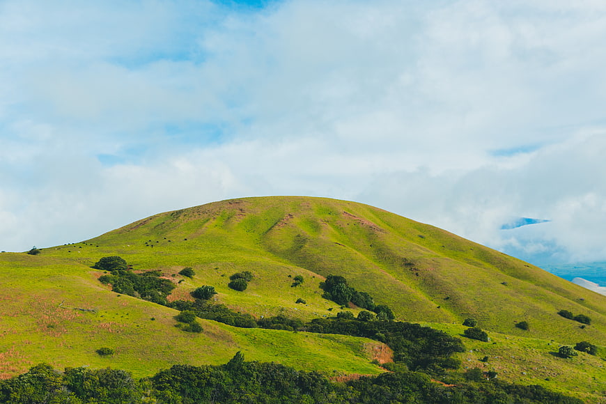 Lush green rolling hills under a cloudy blue sky