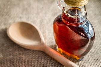 Glass bottle of maple syrup with wooden spoon on rustic linen